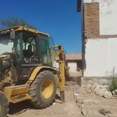 Retroexcavadora en trabajos de demolición junto a una vivienda